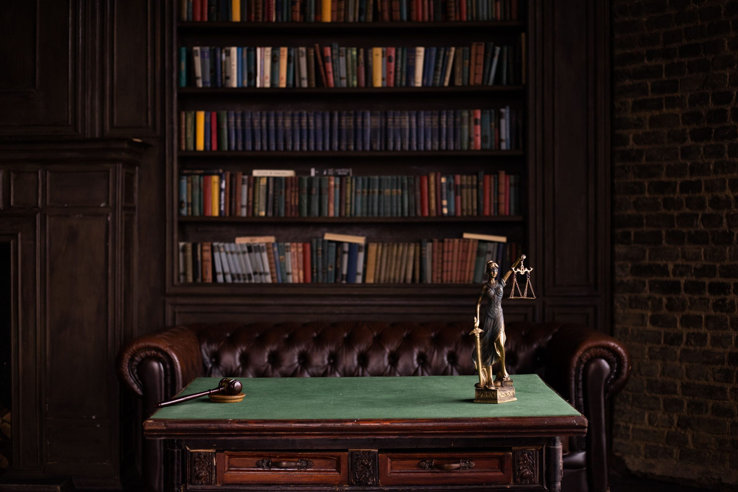 Classic law firm study with shelves of legal books, a gavel, and a Lady Justice figurine on a green table