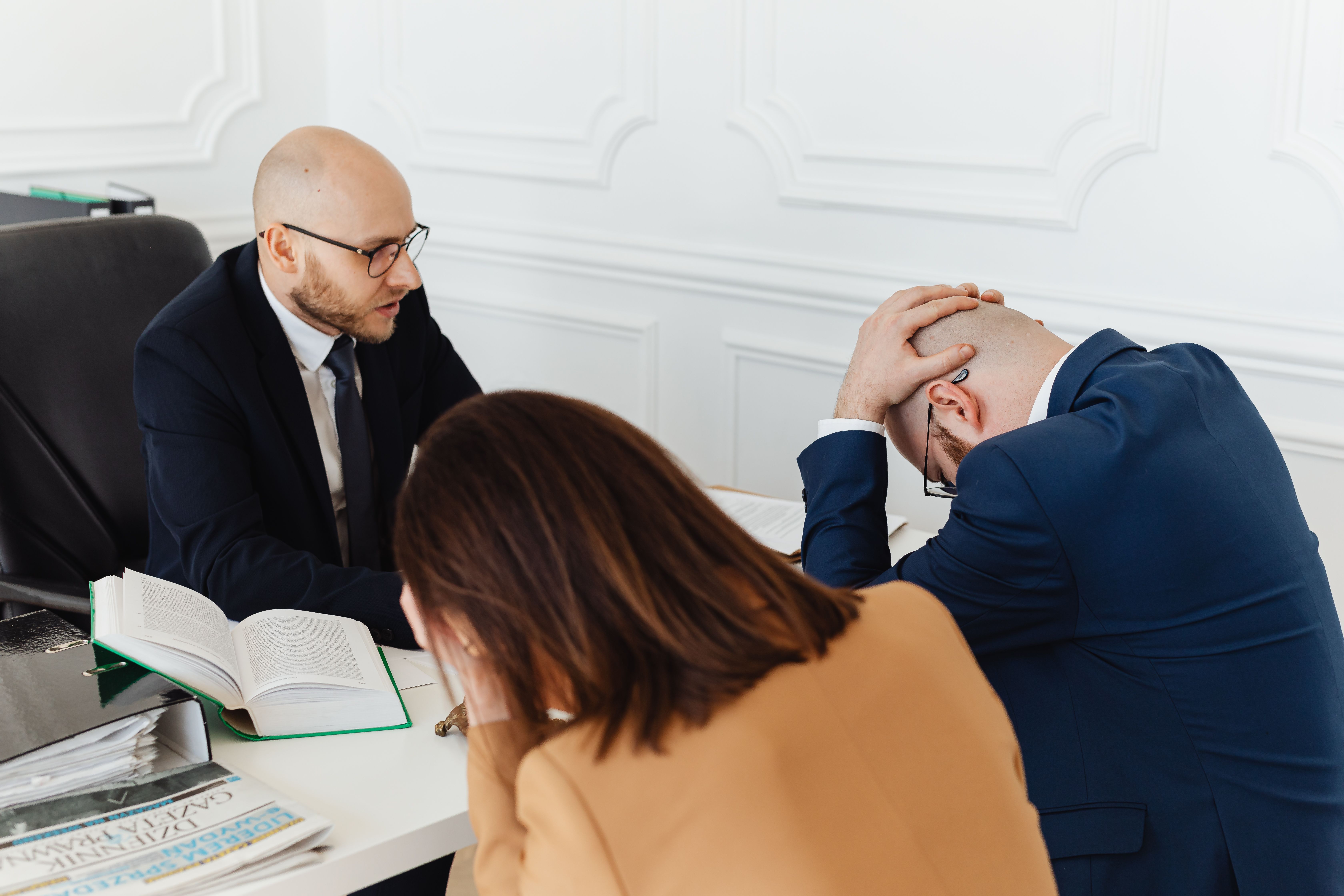 Legal professionals in a tense meeting at a law office with open documents spread across the desk