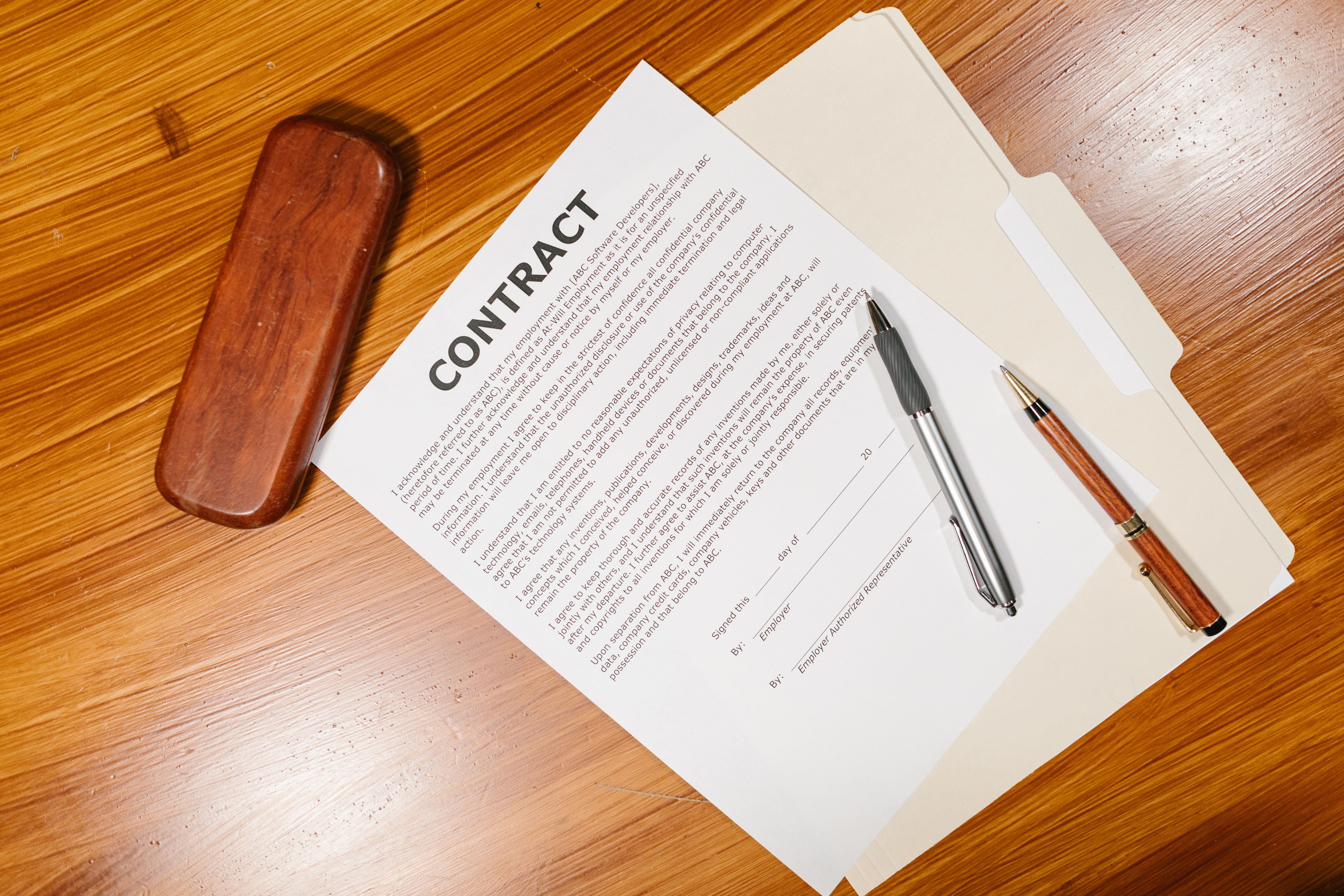 High-angle view of a legal contract document with pens and a case on a wooden table