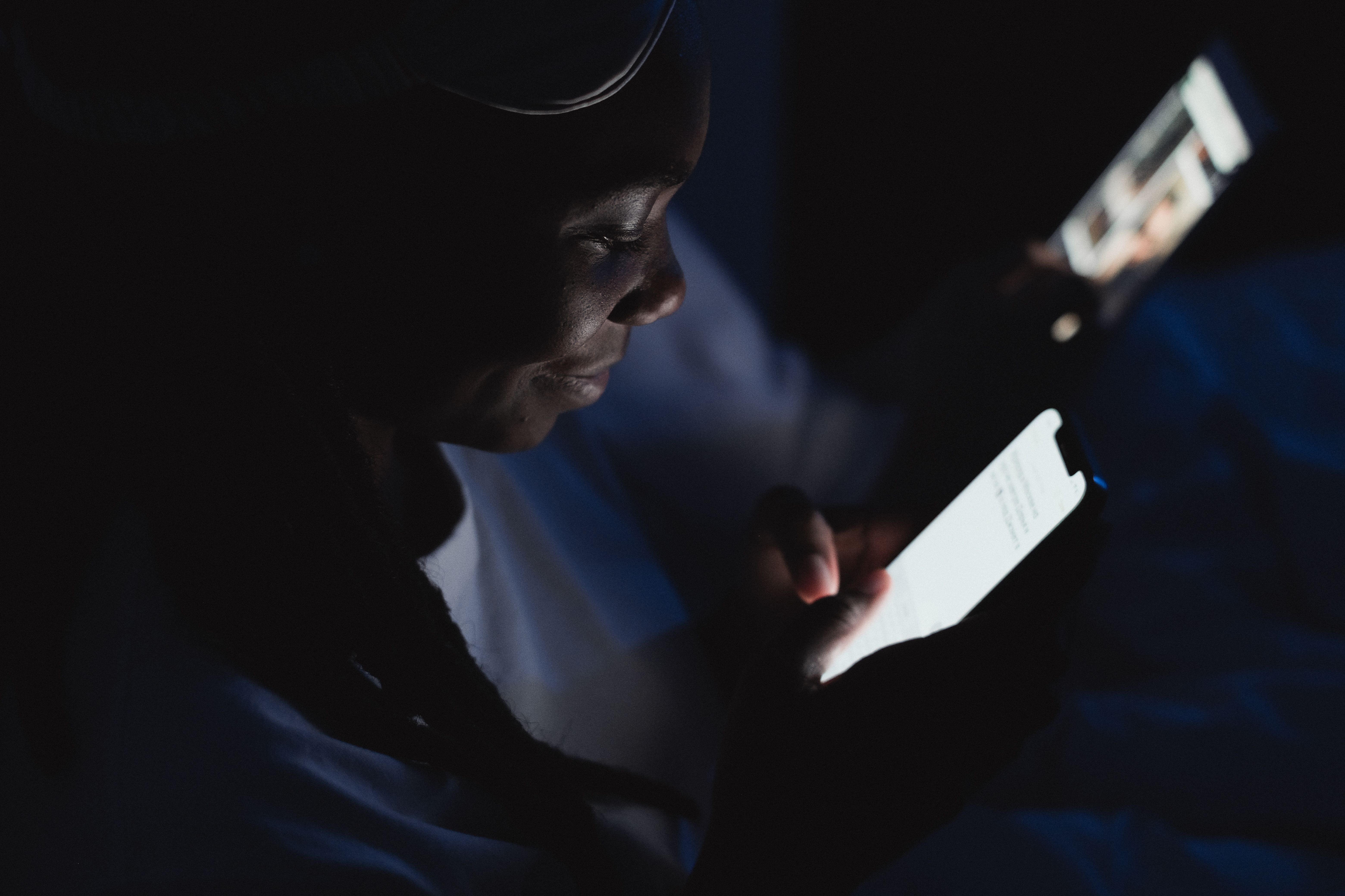 Close-up of a woman reading on her smartphone in a dark room, her face illuminated only by the screen glow.
